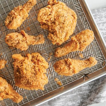 Golden-brown breaded chicken pieces on Nordic Ware nonstick grid inside aluminum half sheet pan