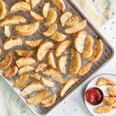 Golden roasted potato wedges on Nordic Ware nonstick grid with aluminum half sheet pan, wedges plated beside