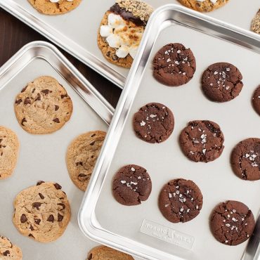 Three Nordic Ware aluminum sheet pans with baked cookies: chocolate chip, double chocolate with sea salt, and mixed varieties