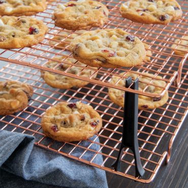 Freshly baked chocolate chip cookies cooling on Nordic Ware copper-colored stackable wire cooling grids