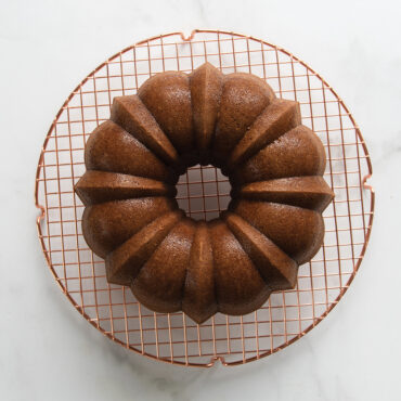 Golden brown bundt cake on Nordic Ware round copper cooling grid, overhead view on marble surface