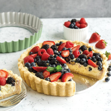 Fresh berry tart with custard filling in Nordic Ware fluted tart pan, slice removed showing creamy interior