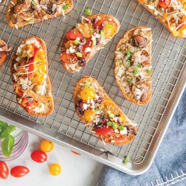 Toasted bruschetta with colorful toppings on Nordic Ware cooling grid in aluminum sheet pan