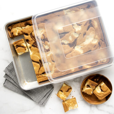 Nordic Ware aluminum high-sided sheet cake pan with clear lid, containing golden brown blondies