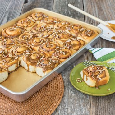 Nordic Ware aluminum high-sided sheet pan with golden cinnamon rolls topped with nuts and glaze