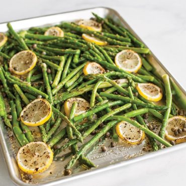 Roasted asparagus spears with lemon slices on Nordic Ware aluminum sheet pan, golden-brown and seasoned