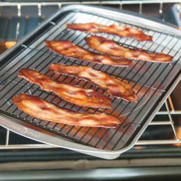 Nordic Ware aluminum oven crisp baking tray with golden-brown cooked bacon strips arranged in rows