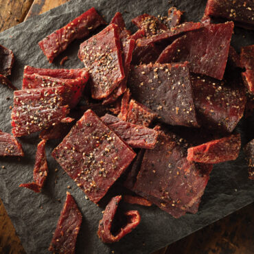 Strips of dark brown beef jerky arranged on Nordic Ware aluminum oven crisping tray with perforated surface