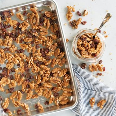 Roasted walnuts and cranberries on Nordic Ware aluminum sheet pan with glass jar and spoon nearby