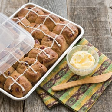 Nordic Ware aluminum quarter sheet pan with clear lid containing six golden Hot Cross Buns with cross icing
