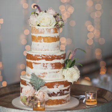 Three-tier white wedding cake with pink roses and lit candles, displayed on tiered cake stands from Nordic Ware set