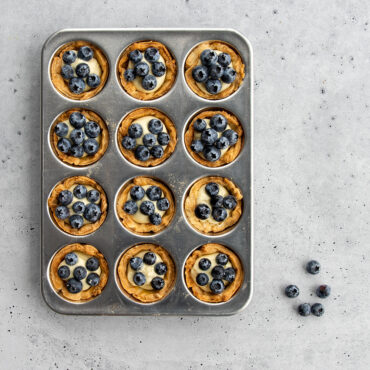 Nordic Ware natural aluminum 12-cup muffin pan with golden baked mini tarts in each cavity