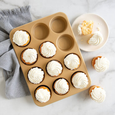 Nordic Ware aluminum muffin pan with 12 cavities filled with frosted vanilla cupcakes, natural finish