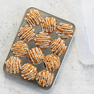 Nordic Ware aluminum 12-cavity muffin pan with clear domed lid, containing freshly baked golden muffins