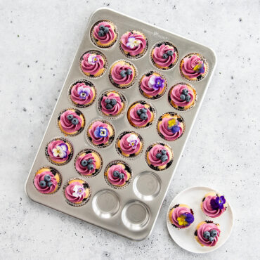 Nordic Ware aluminum 24-cavity petite muffin pan with small frosted cupcakes, natural finish