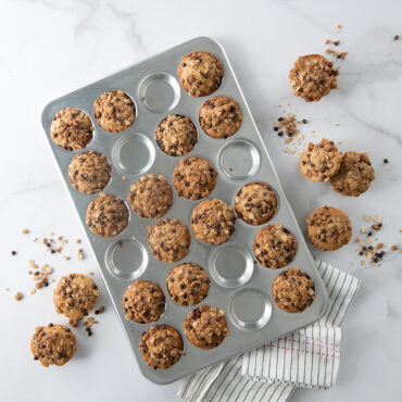 Nordic Ware aluminum 24-cavity petite muffin pan with golden brown mini muffins in natural silver finish