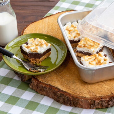Sliced brownies on white plate next to Nordic Ware Naturals aluminum 9-inch square cake pan with lid