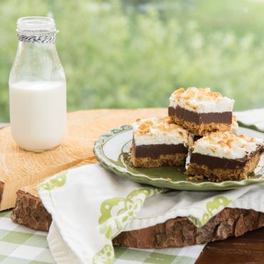 S'mores bars with graham cracker crust and marshmallow topping cut into squares on white plate, baked in Nordic Ware aluminum square pan
