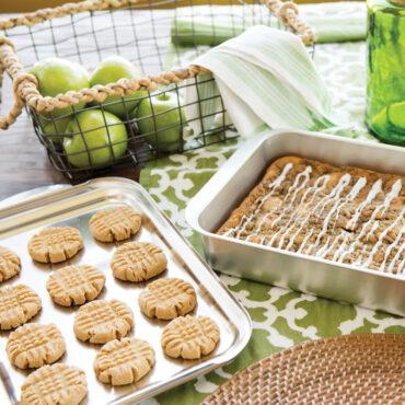 Nordic Ware aluminum covered baking pan with apple streusel cake, golden cookies cooling on lid
