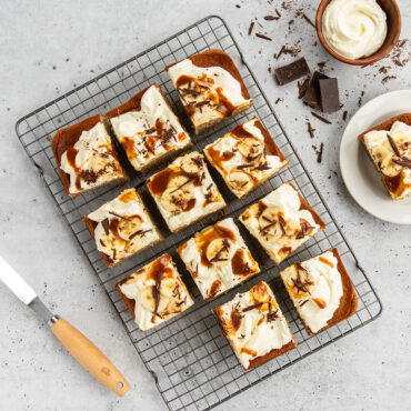 Frosted chocolate brownies cut into squares on wire cooling rack, topped with nuts and cream cheese swirls