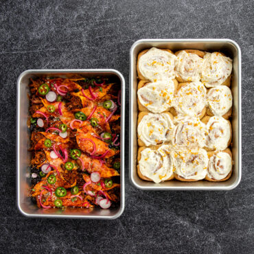Two Nordic Ware aluminum 9x13 rectangular cake pans: one with spicy enchiladas, one with cinnamon rolls