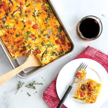 Golden egg bake with vegetables in Nordic Ware aluminum 9x13 rectangular cake pan, slice served on white plate
