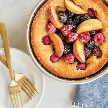 Golden baked cake with fresh peach slices, raspberries and blackberries in Nordic Ware aluminum round pan