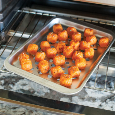 Golden brown tater tots arranged on Nordic Ware aluminum crisping sheet inside toaster oven