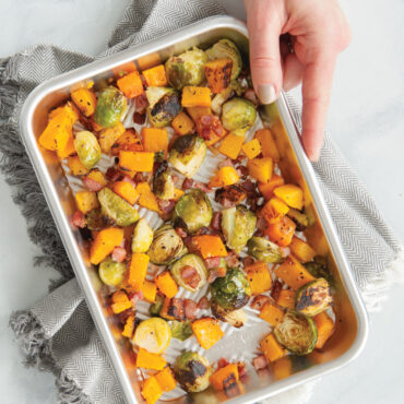 Hand holding Nordic Ware Prism aluminum eighth sheet pan with colorful roasted vegetables using kitchen towel