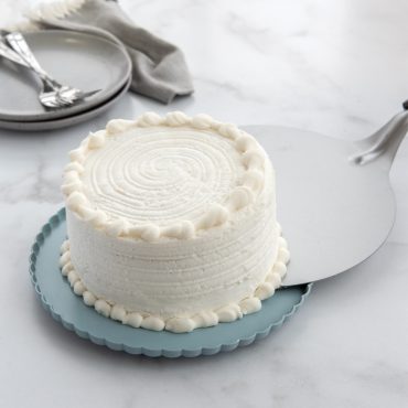 Two-tier aluminum dessert stand with clear dome lid displaying layered cake on bottom tier, silver finish