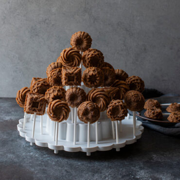 White three-tiered circular display stand holding colorful round cake pops on sticks, arranged on each level