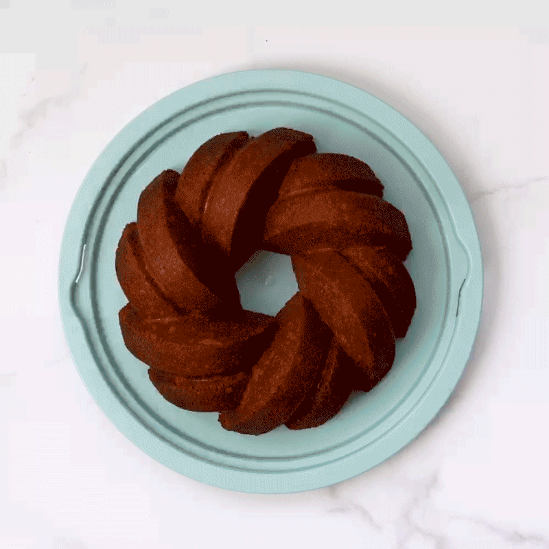 Hand placing clear plastic dome cover over Nordic Ware translucent bundt cake keeper containing golden bundt cake