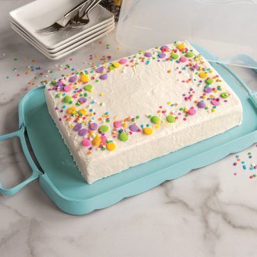 Nordic Ware white plastic cake carrier with clear lid, holding decorated birthday cake with colorful frosting