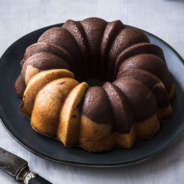 Golden marbled bundt cake with swirled chocolate and vanilla layers on white serving platter