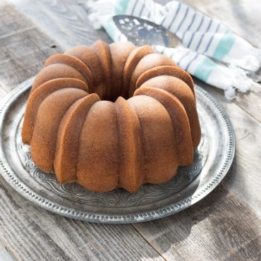 Golden bundt cake with detailed fluted ridges displayed on white pedestal cake stand