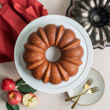 Nordic Ware bronze bundt pan next to golden bundt cake on white platter with autumn table setting