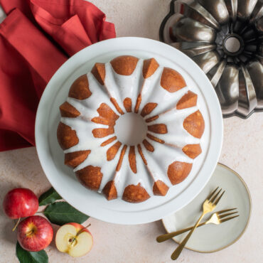 Iced bundt cake on white platter next to Nordic Ware bronze cast aluminum bundt pan