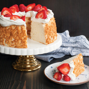 Sliced angel food cake with white frosting on Nordic Ware aluminum tube pan, showing light airy texture
