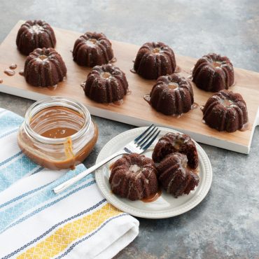 Chocolate glazed mini bundt brownies with fluted design on wooden board, jar of caramel sauce nearby