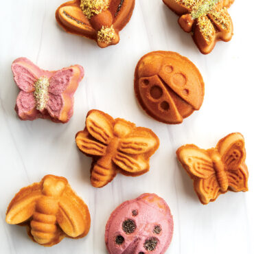 Golden mini cakes shaped like butterflies, ladybugs, and bees from Nordic Ware Backyard Bugs pan, decorated with colorful icing