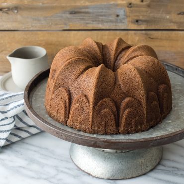 Golden brown spice cake baked in Nordic Ware Fleur-de-Lis bundt pan on ceramic cake stand