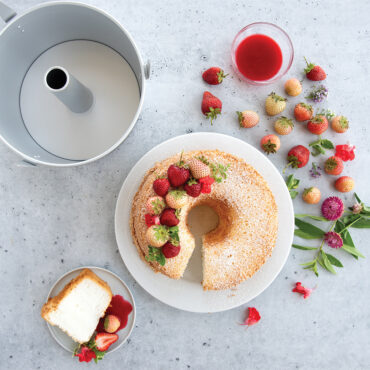 Nordic Ware aluminum angel food cake pan with removable cone, natural finish, displayed with finished powdered sugar cake and strawberries
