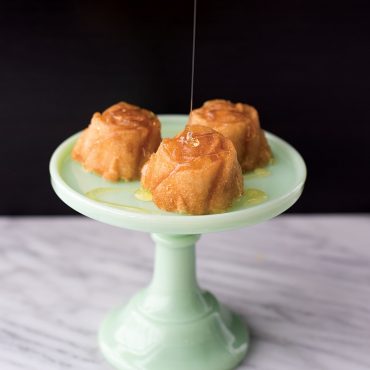 Three golden vanilla cakes with rose-shaped details on mint green pedestal stand, drizzled with honey