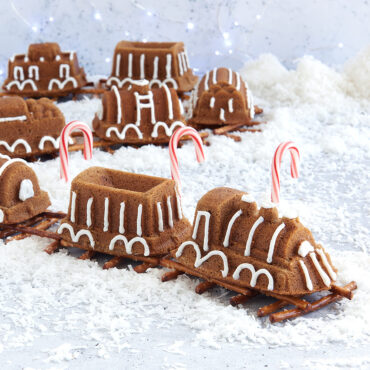 Decorated train-shaped cake with colorful frosting, baked in Nordic Ware train cake pan, arranged on pretzel track