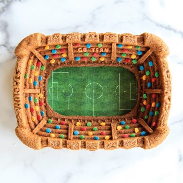 Golden bundt cake baked in Nordic Ware aluminum stadium pan, showing tiered seating design with colorful sprinkles