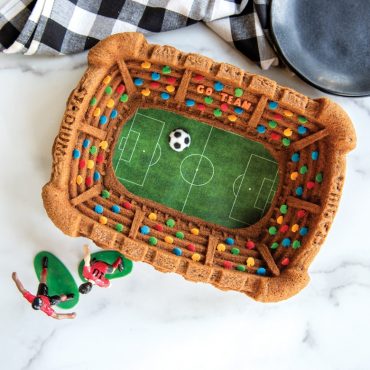 Nordic Ware Stadium Bundt pan with soccer-themed cake, detailed stadium architecture, gray aluminum finish