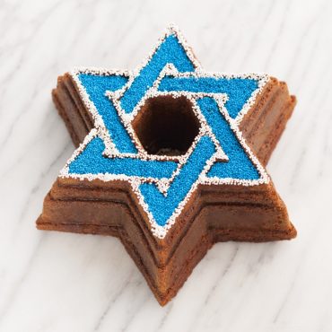 Chocolate bundt cake with white icing drizzle baked in Nordic Ware Star of David shaped pan on marble surface