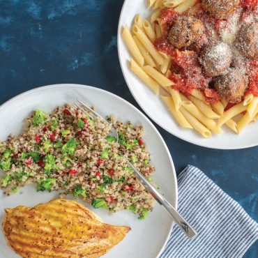 Two Nordic Ware white microwave-safe plates with quinoa salad and grilled chicken, pasta with meatballs
