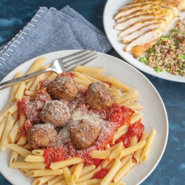 White Nordic Ware microwave-safe plate with penne pasta, marinara sauce, meatballs and parmesan cheese