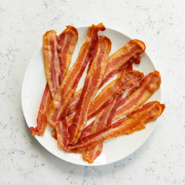 Crispy golden-brown bacon strips arranged on white plate, cooked to perfect doneness with caramelized edges